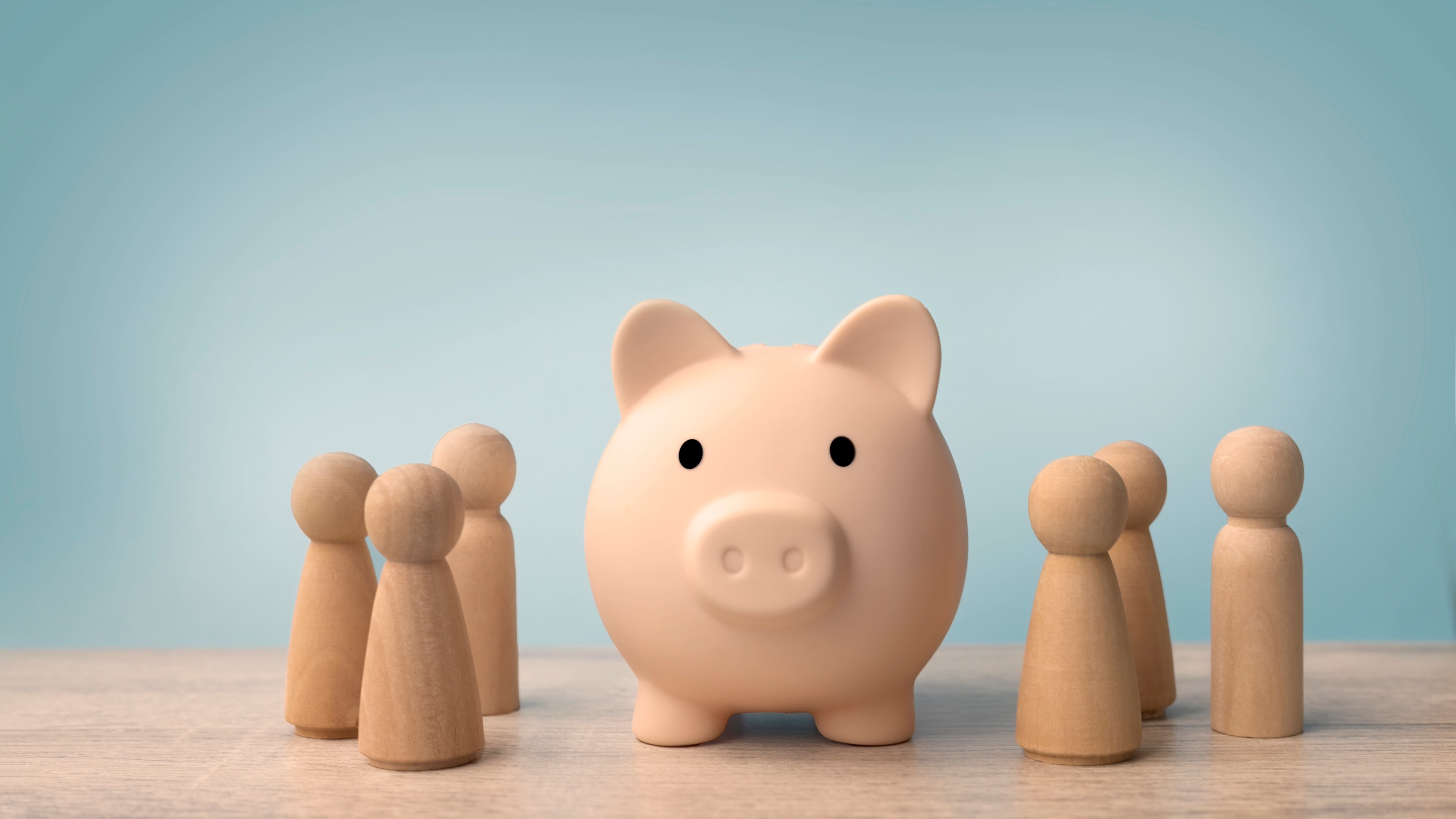 Small wooden figures representing a family standing together around a central piggy bank.