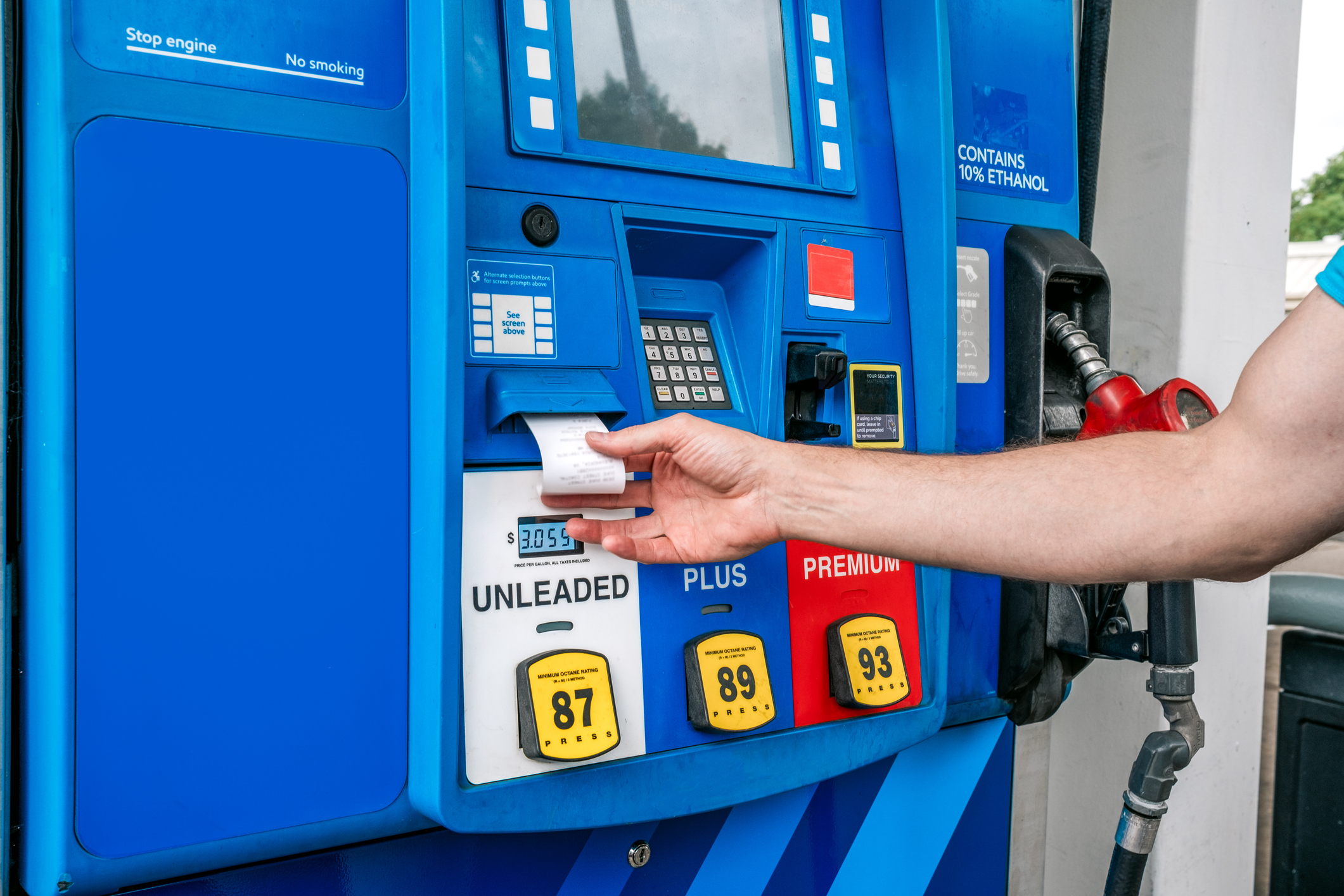 A driver taking a paper receipt from the dispenser at a modern gas station pump.