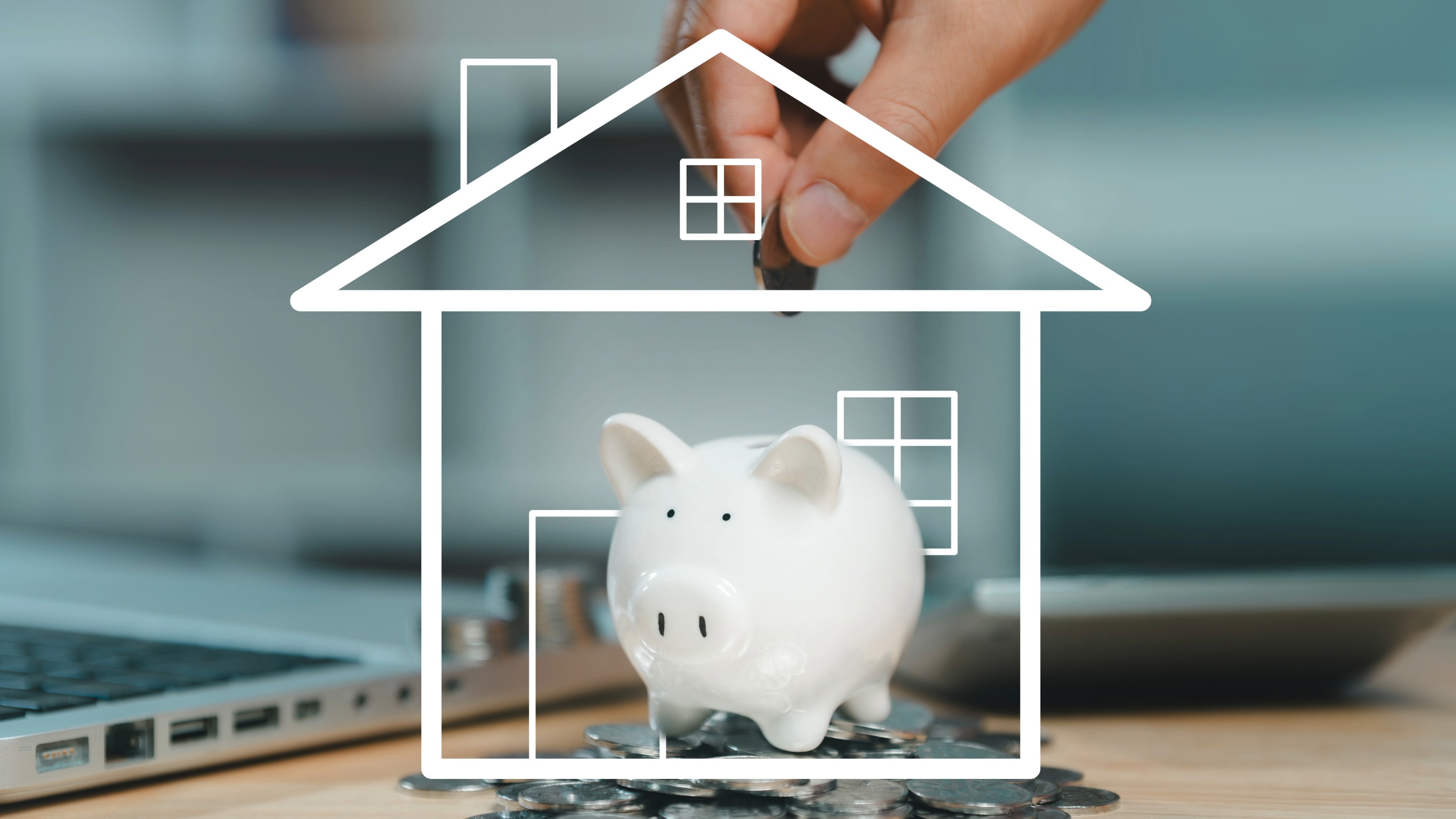 A hand putting a coin into a piggy bank shaped like a house outline.
