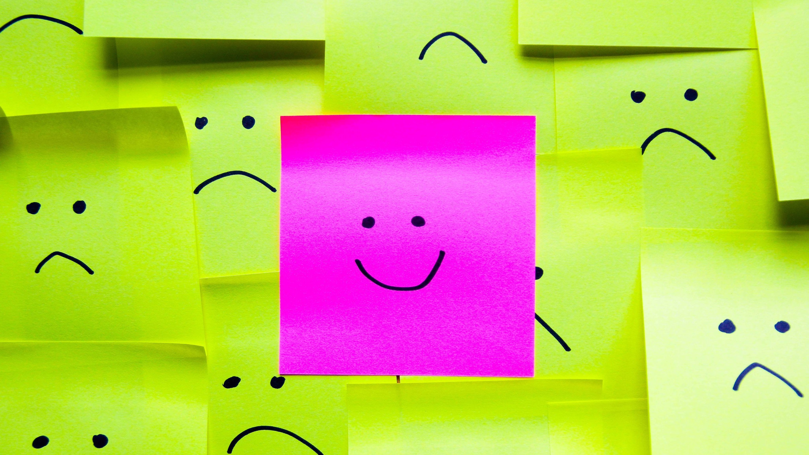A pink post-it with a smiley face surrounded by yellow post-its with sad faces.