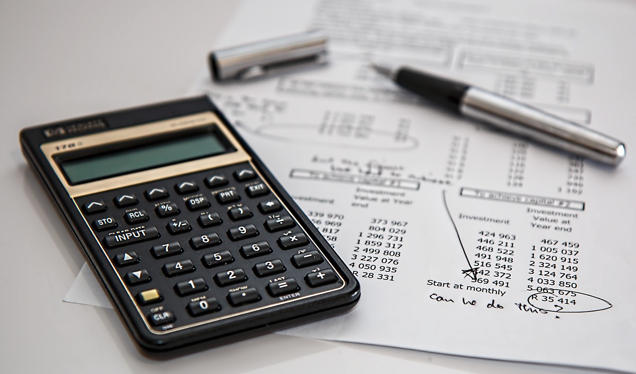 Close up of financial documents, a calculator, and reading glasses on a desk