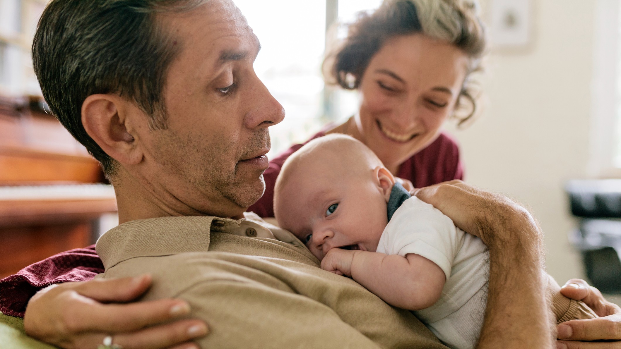 A close-up of a grandmother and grandfather in their 50s smiling and embracing their newborn grandchild.