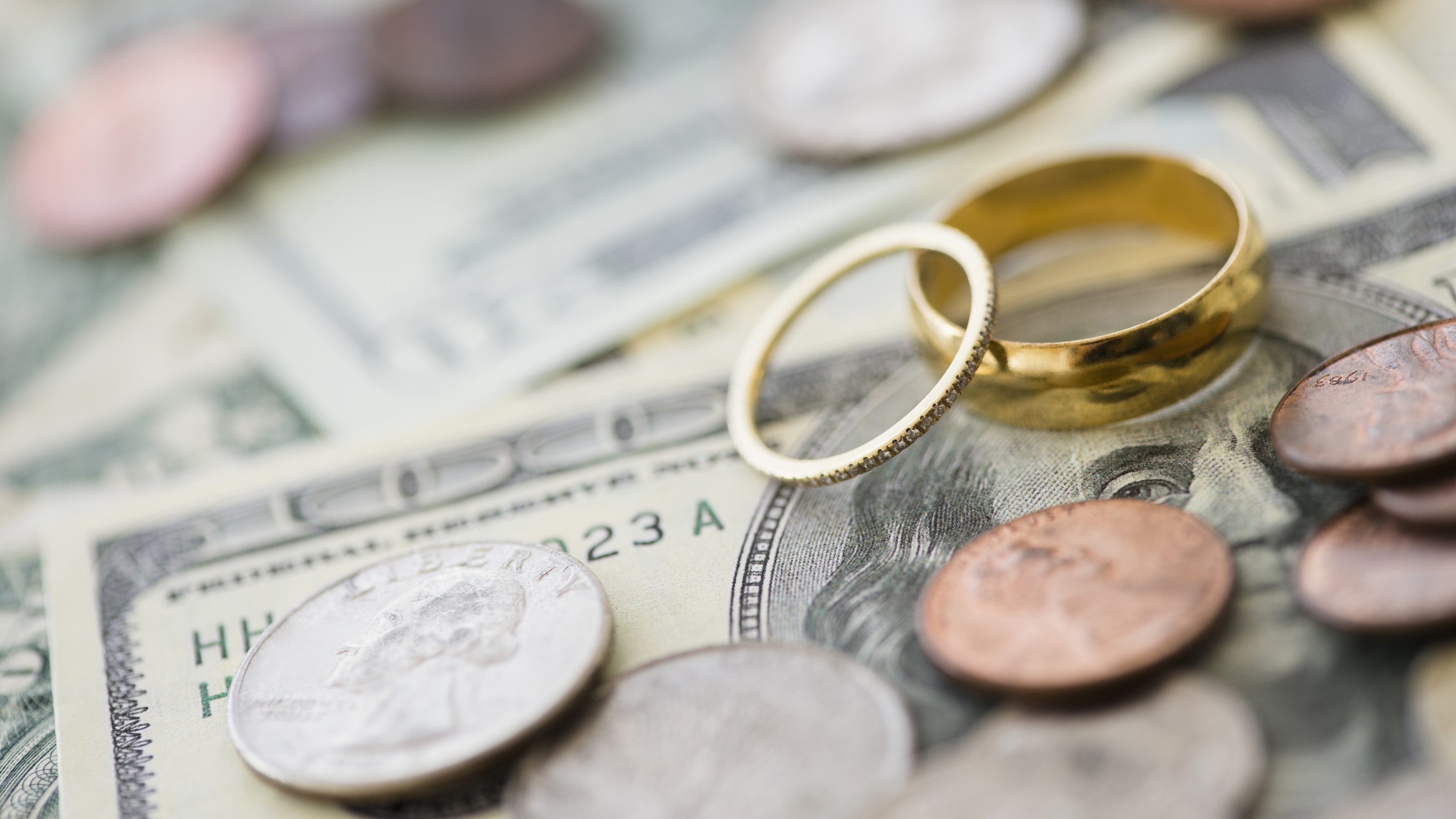 Close up of wedding rings placed on top of a stack of cash and loose coins.