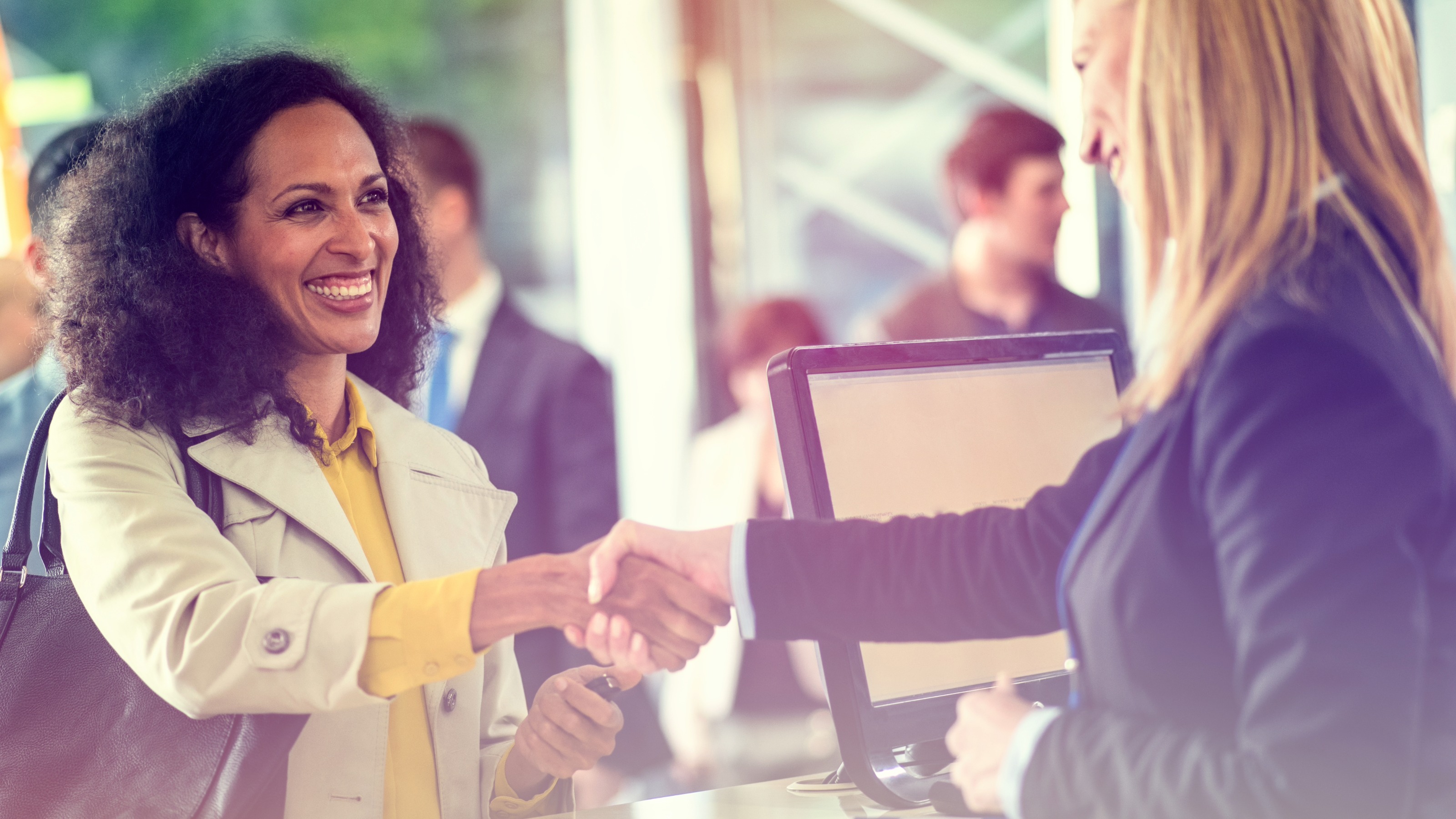 A bank teller and a customer shaking hands over a counter in a sunlit, modern bank branch.
