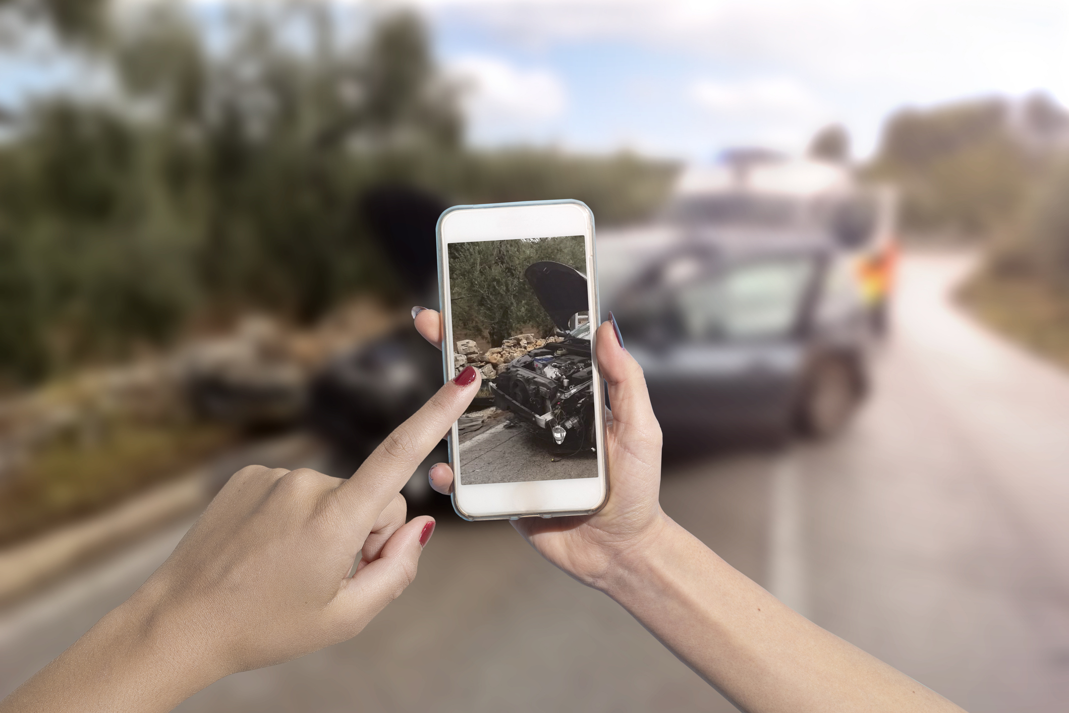 A person using a smartphone to take photos of vehicle damage at a crash site.