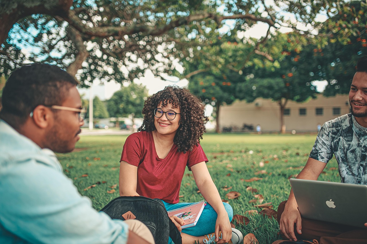 A young university student using a laptop on a sunny outdoor campus.